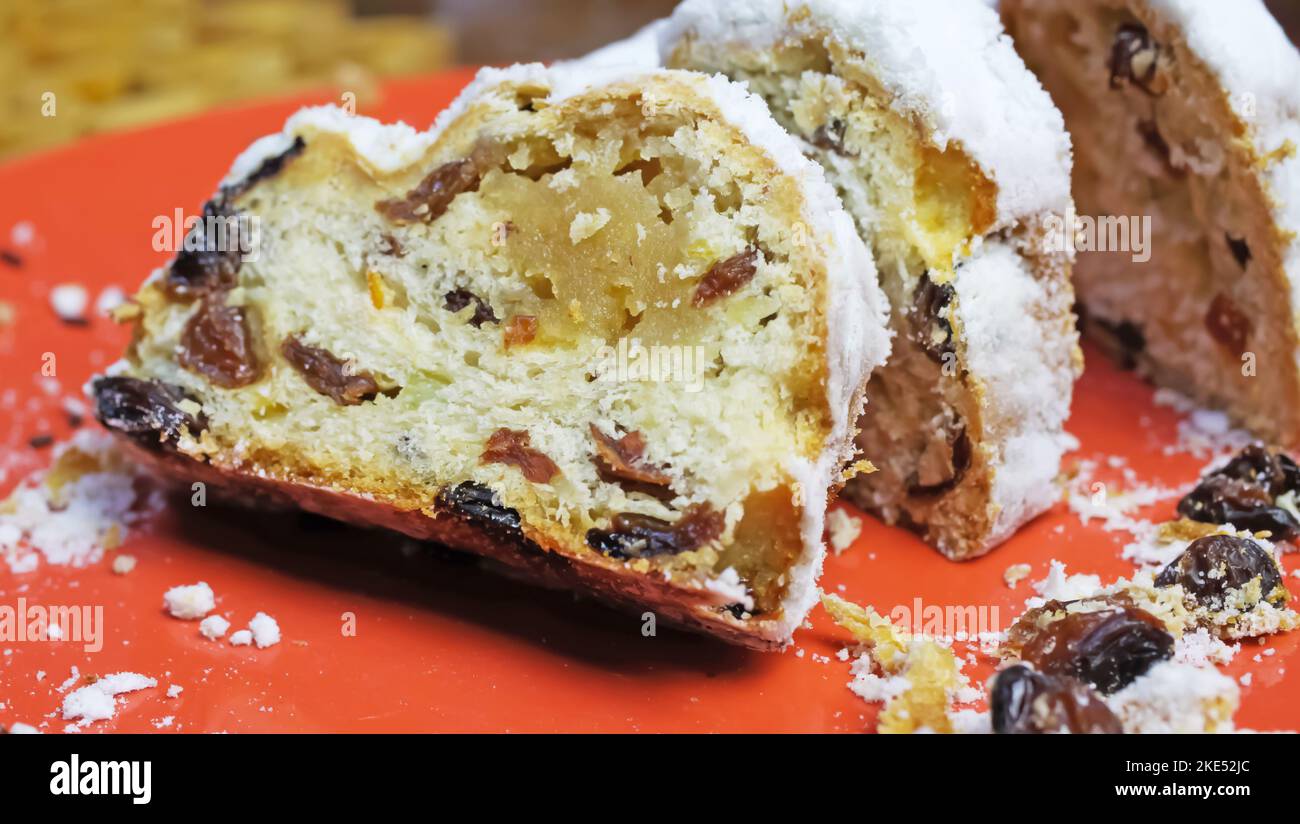 Gros plan de christstollen tranché isolé avec des raisins secs, du sucre blanc en poudre et du massepain sur la plaque rouge Banque D'Images