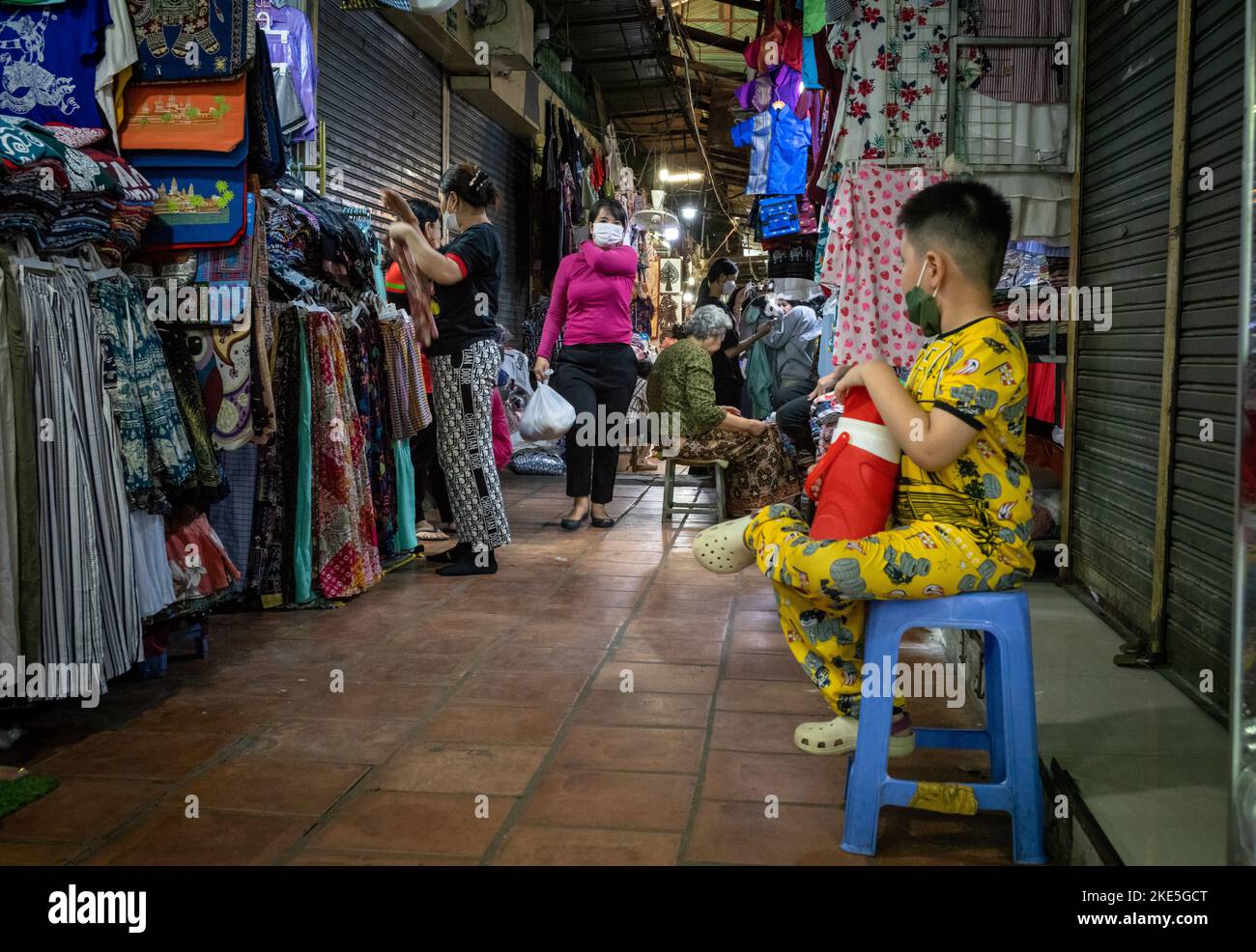 Un jeune garçon vêtu de pyjamas jaunes est assis sur un tabouret dans une ruelle du marché russe de Phnom Penh, au Cambodge. Banque D'Images