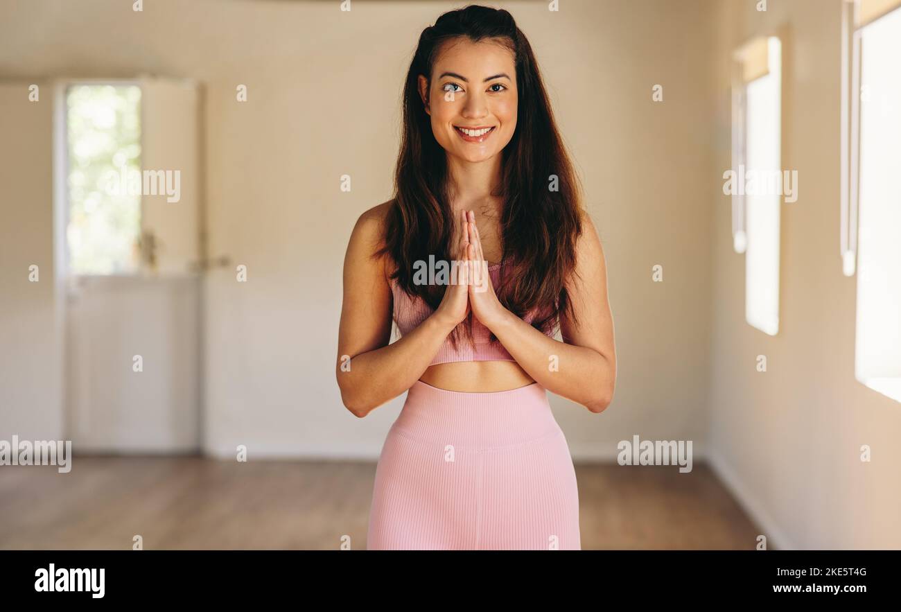 Portrait d'une jeune femme heureuse souriant à l'appareil photo tout en se tenant dans la pose de prière. Jeune femme gaie pratiquant le hatha yoga dans un studio de yoga. Banque D'Images
