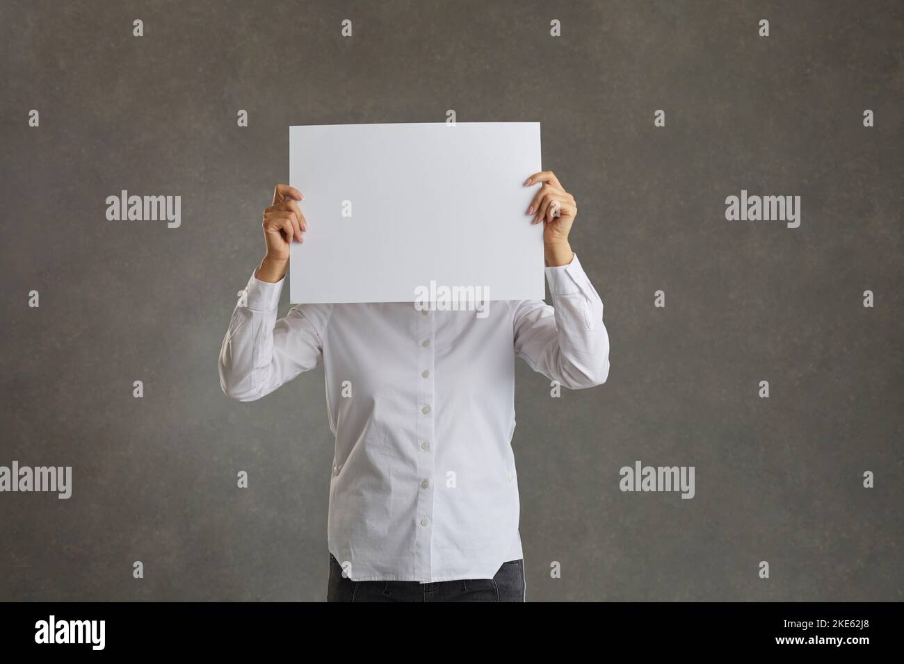 Man tient une feuille blanche de papier vierge devant son visage, espace de copie. Banque D'Images