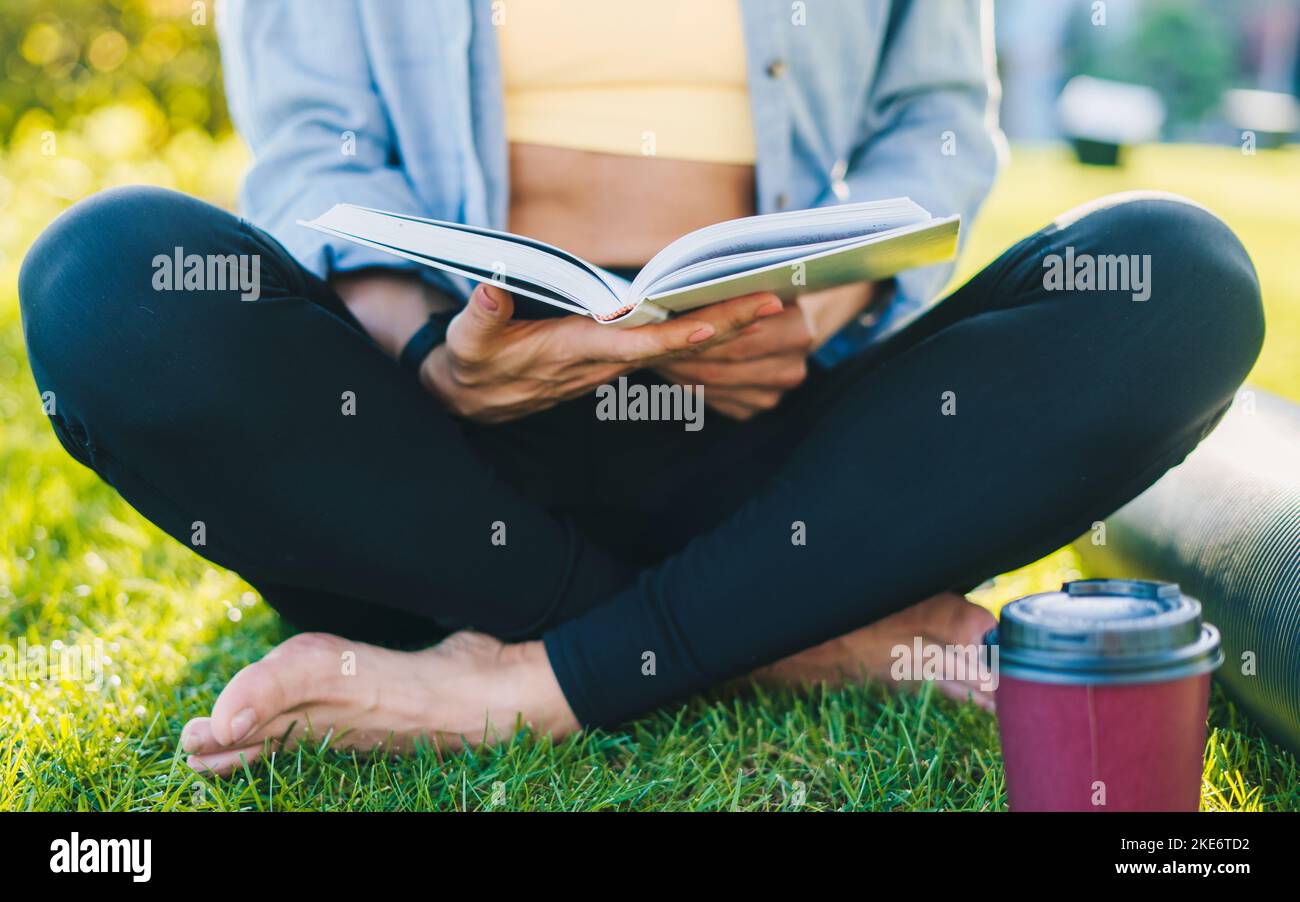 Les mains d'une femme non reconnue tenant un livre dans ses mains qu'elle lit après son entraînement matinal dans le parc. Voyages, vacances, vacances Banque D'Images