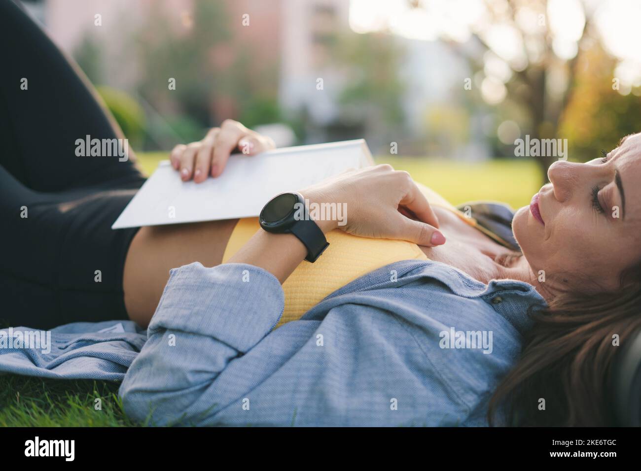 Femme sportive de race blanche couchée d'herbe après qu'elle a fatigué pour avoir lu un livre le matin. Sommeil sain. Nature été. Banque D'Images