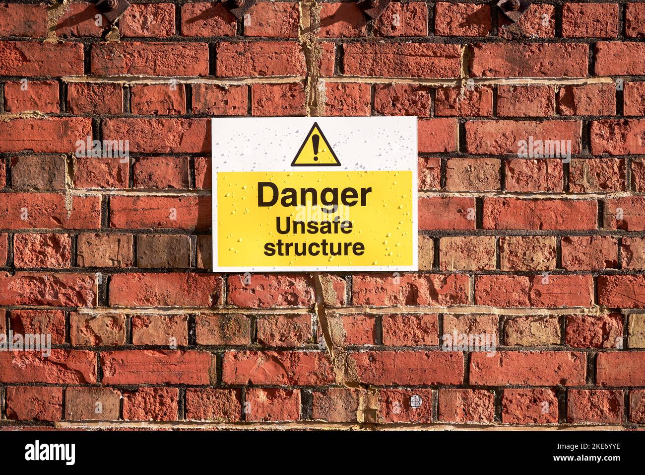 Danger : panneau d'avertissement de structure dangereuse fixé au mur en brique rouge Banque D'Images