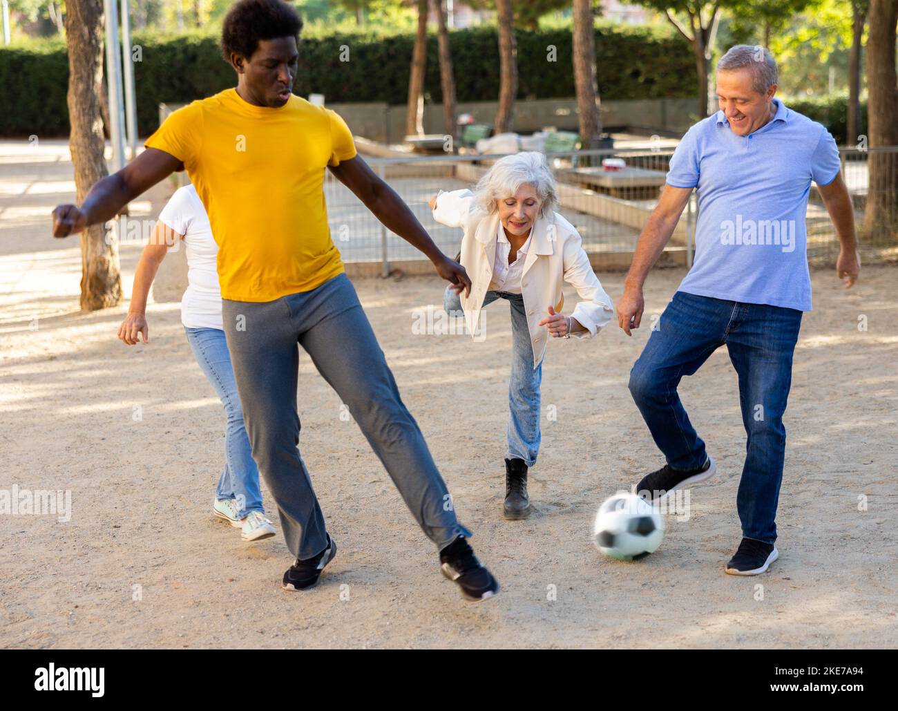 Joyeux amis multinationaux jouant au football sur un terrain de jeu sablonneux lors d'une chaude soirée de printemps Banque D'Images