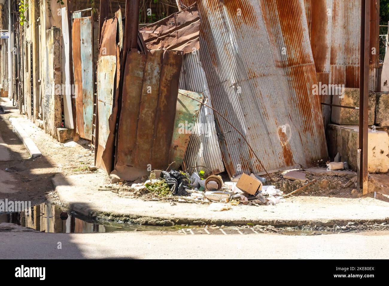 Trottoir sale et clôture métallique en panne dans un coin de la ville. Il y a des déchets et de l'eau stagnante. Banque D'Images