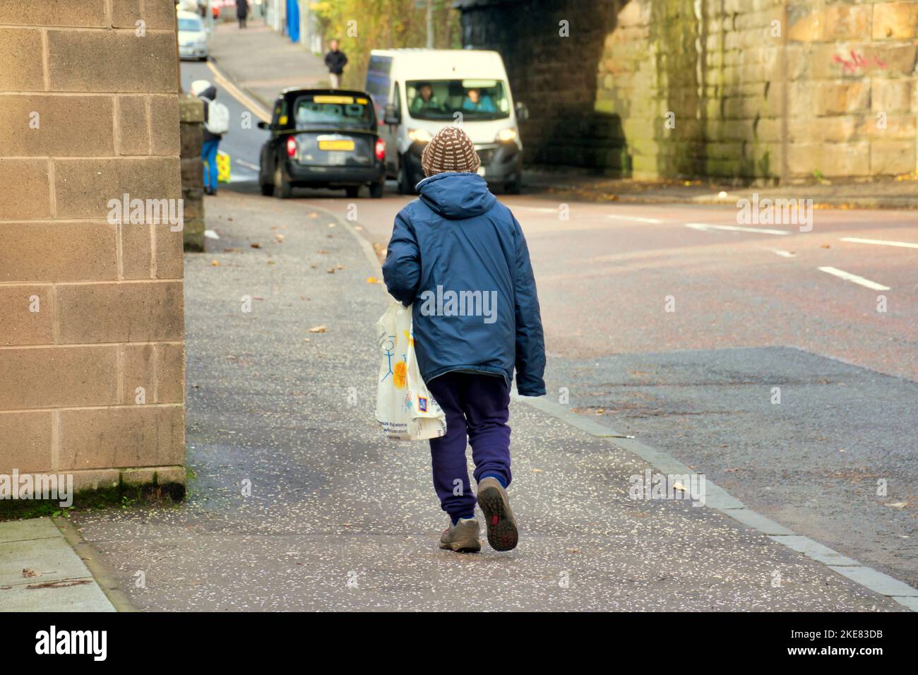 Homme sans cheveux avec sac de shopping en plastique marchant sur Maryhill Road Banque D'Images