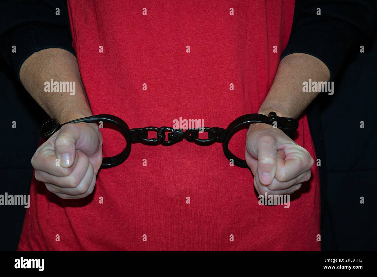 Photo d'une paire de mains de femmes avec des manilles en fer devant une chemise rouge. Banque D'Images