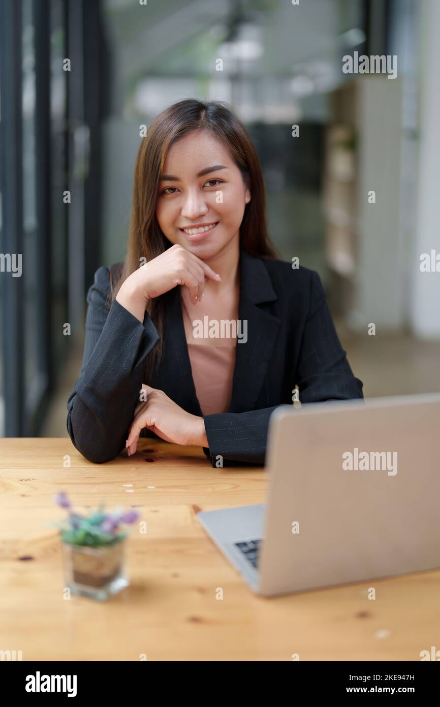 Portrait d'une belle femme d'affaires asiatique en costume habillé assis à son bureau avec ordinateur portable dans le bureau Banque D'Images