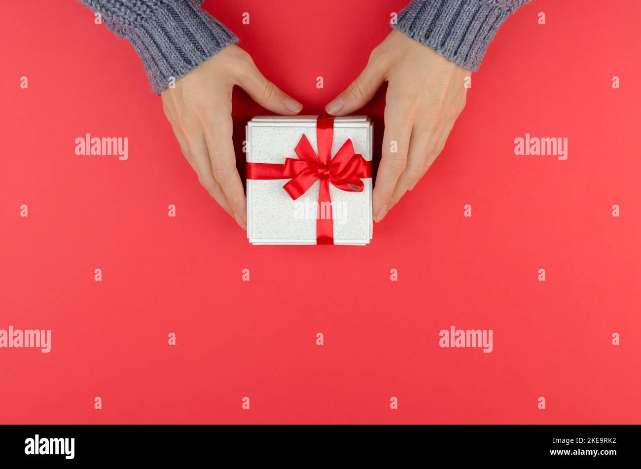 Boîte cadeau dorée entre les mains des femmes sur fond rouge Banque D'Images