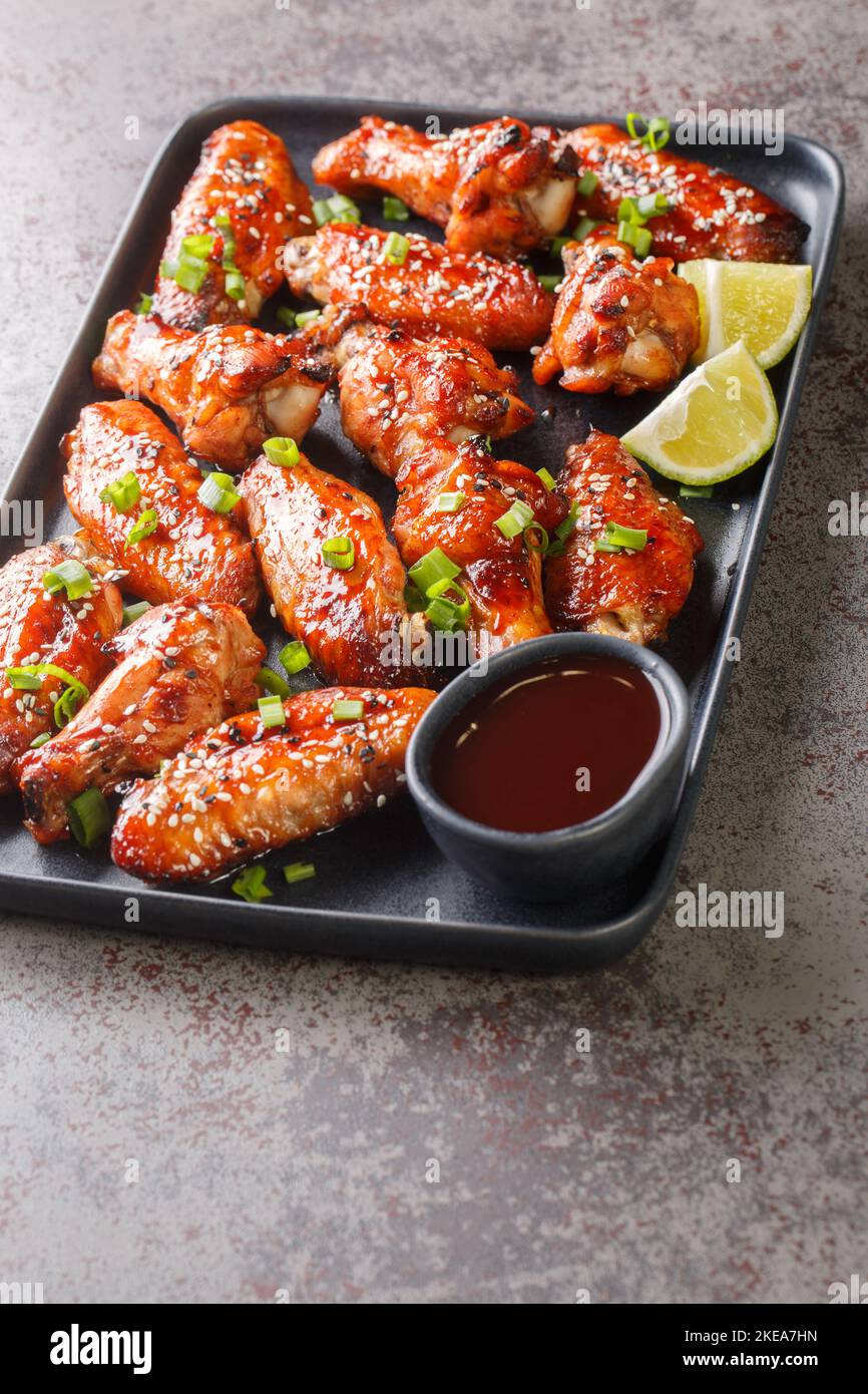 Ailes de poulet au houisin au sésame, à l'oignon vert et à la lime servies avec de la sauce dans une assiette sur la table. Verticale Banque D'Images