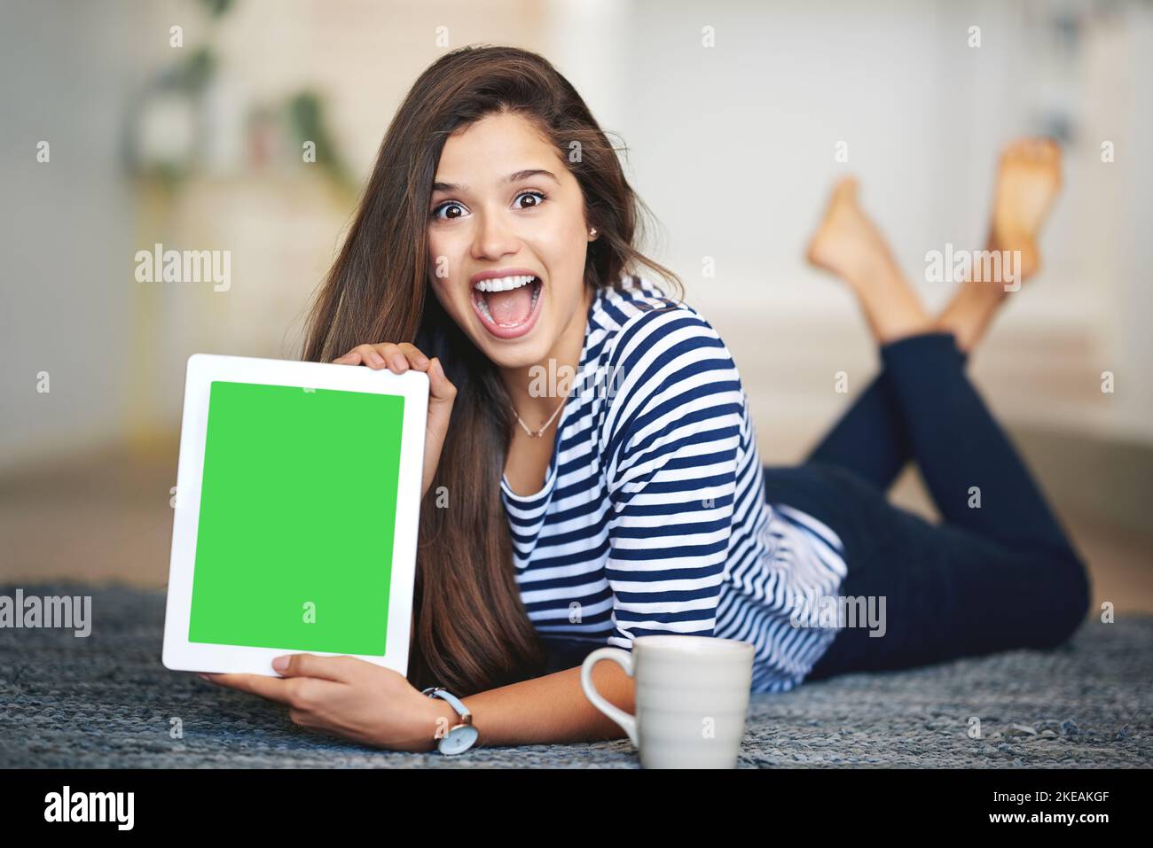 Pouvez-vous croire ce site.Portrait d'une jeune femme ecstatique couchée sur le sol à la maison tenant une tablette numérique avec un écran couleur clé. Banque D'Images