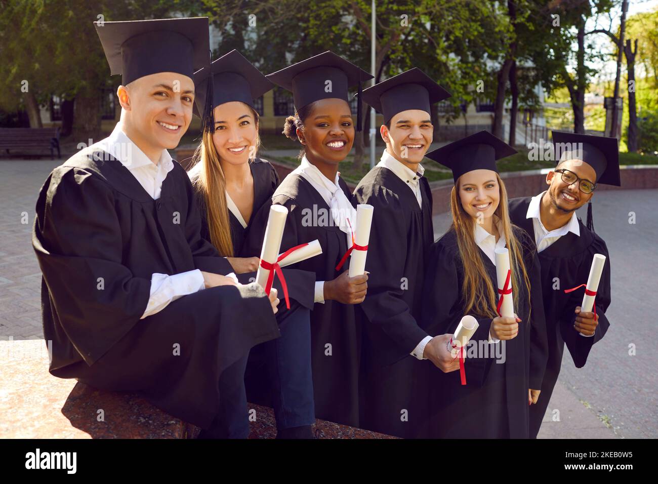 Jeunes gens joyeux diplômé de l'université vêtu d'une robe noire debout dans la rue Banque D'Images