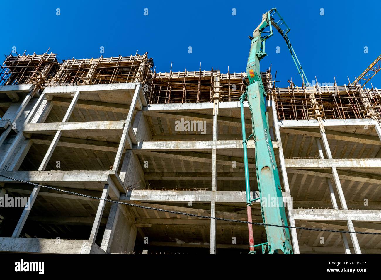 Verser une dalle de béton dans un chantier de construction, avec des grues et des tuyaux de coulée, des ouvriers non reconnaissables sur le toit de ferrobéton. Banque D'Images