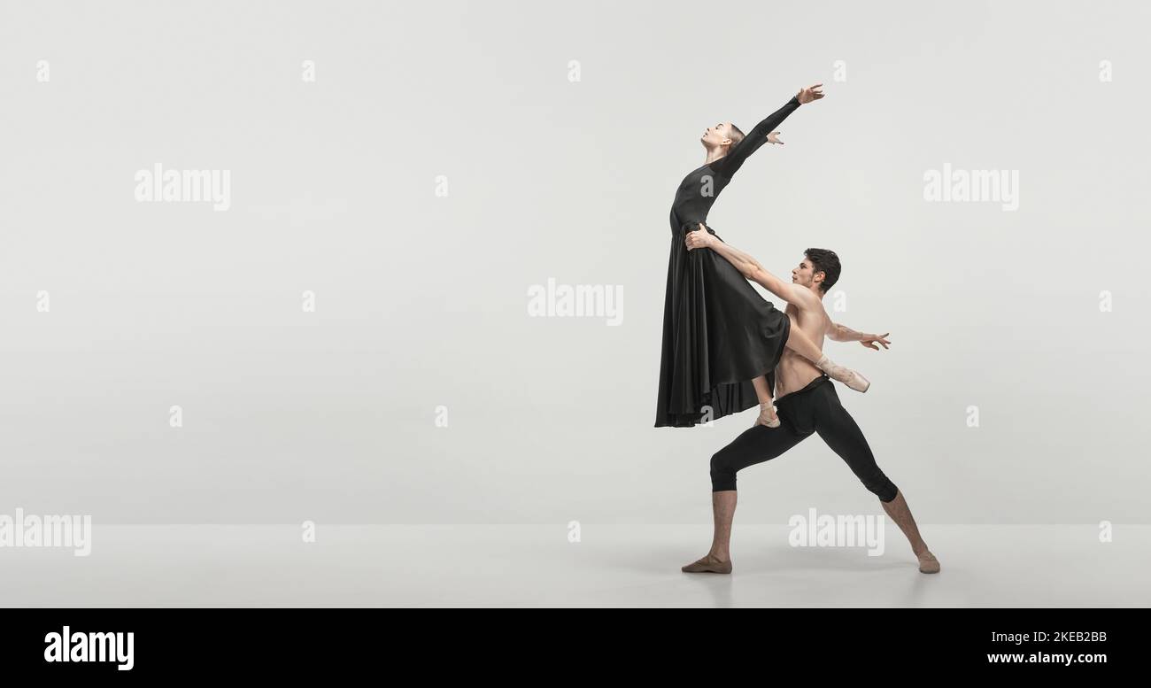 Jeune homme et jeune femme, danseurs de ballet se exécutant isolé sur fond gris studio. Maintien et voler. Circulaire Banque D'Images