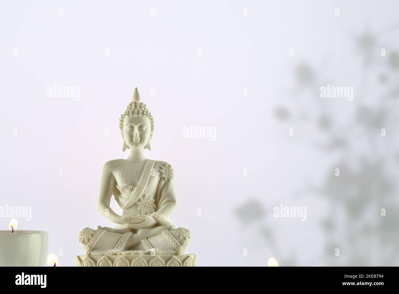 Composition du bouddhisme avec statue de Bouddha blanc et bougies sur fond blanc avec ombres et espace de copie. Vesak, Fête du Bouddha. Santé mentale, détente, Banque D'Images