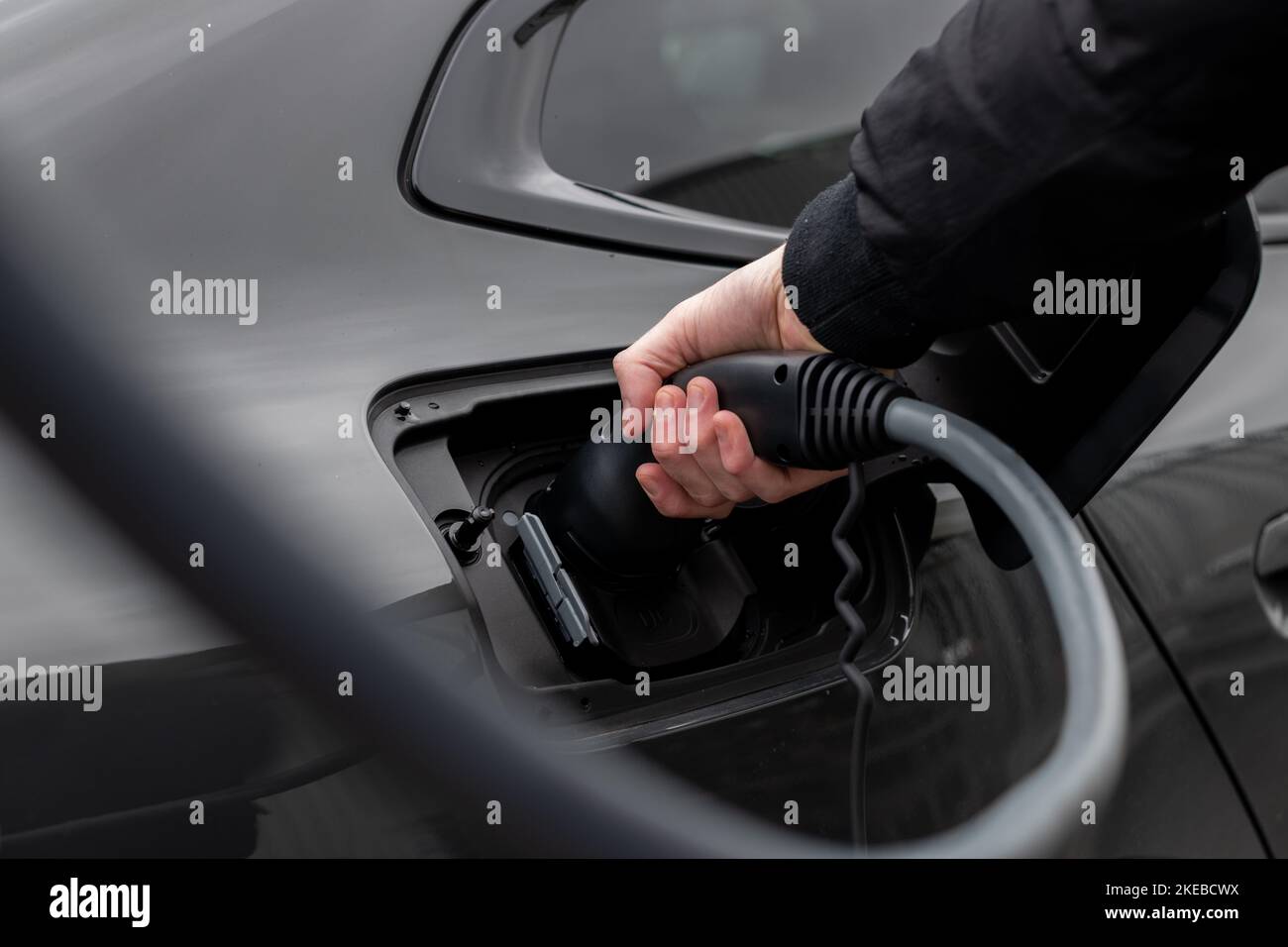 Gros plan de la prise du véhicule électrique arrêt de charge - câble de charge moderne EV avec câble de mise en place homme dans la voiture - image de véhicule à mise au point sélective Banque D'Images