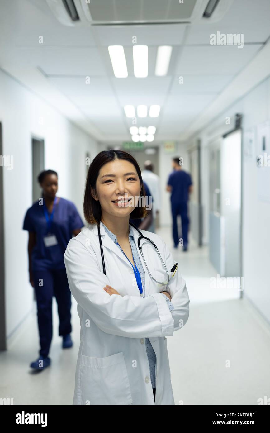 Portrait vertical d'une femme asiatique souriante médecin dans un couloir d'hôpital occupé, espace de copie Banque D'Images