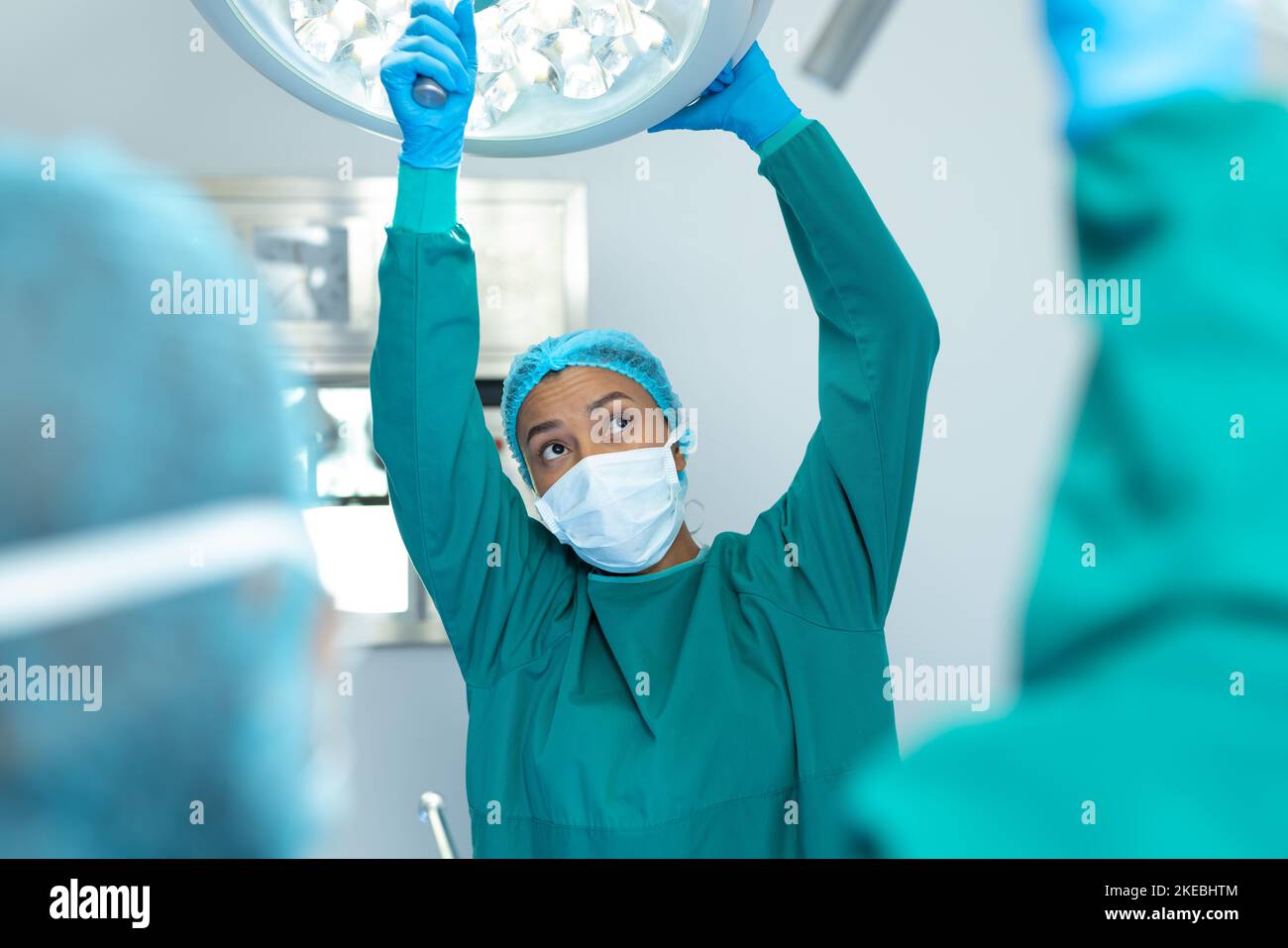 Femme chirurgien biracial ajustant les lumières dans le bloc opératoire pour l'opération Banque D'Images