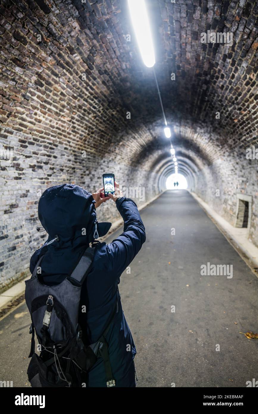 Femme photographiant dans un tunnel sur le chemin de fer de Keswick avec son téléphone mobile, English Lake District. Banque D'Images