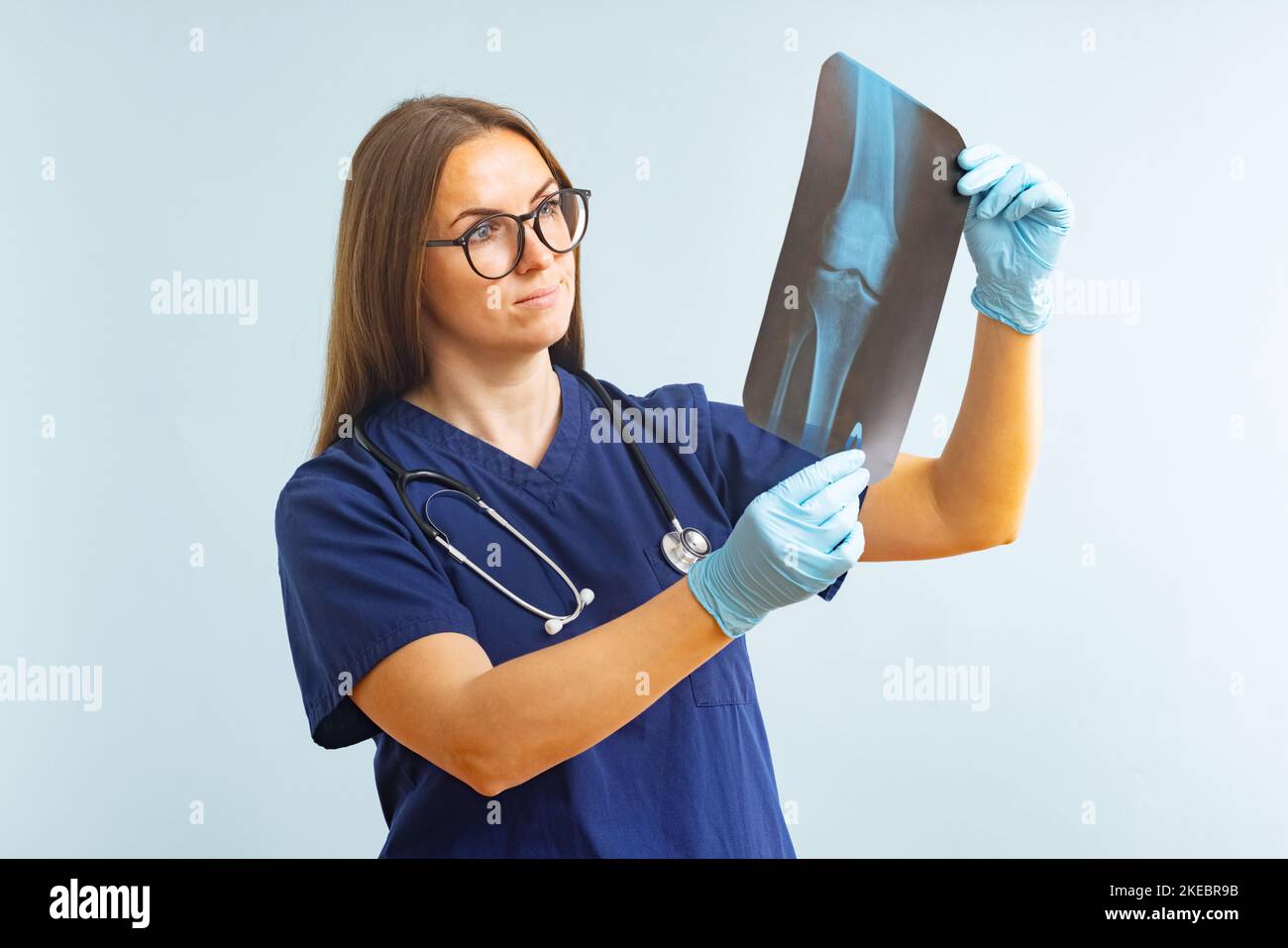 Femme médecin examinant une image de radiographie diagnostiquant une blessure sur fond bleu Banque D'Images