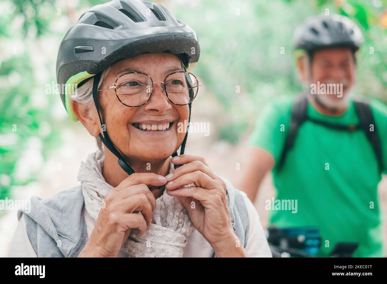 Portrait d'une vieille femme souriant et appréciant la nature en plein air à vélo avec son mari riant. Tête de lit de la femme adulte avec des lunettes se sentant en bonne santé. Un haut-de-compagnie qui met un casque pour faire un voyage avec des vélos. Banque D'Images