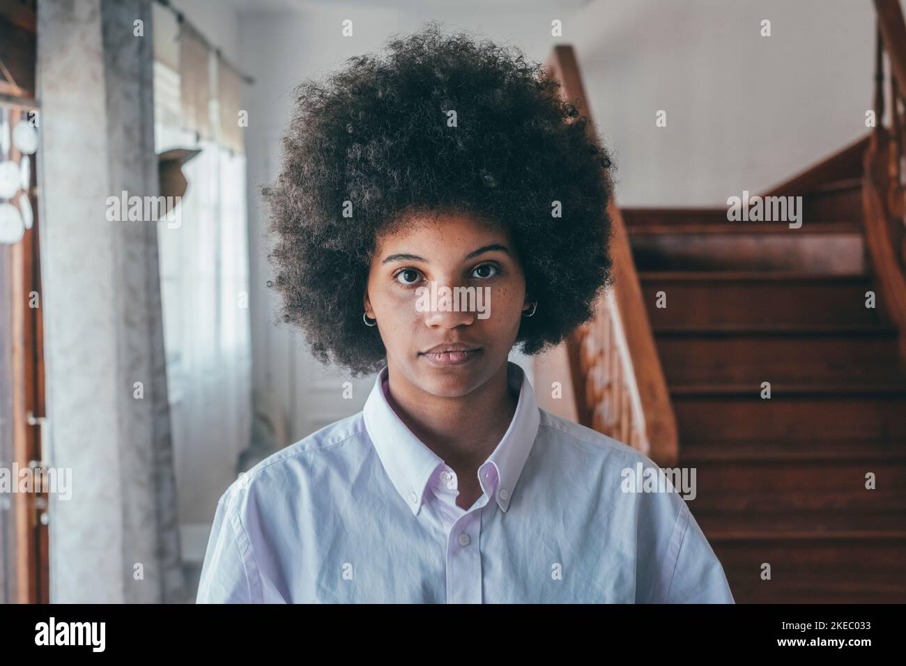 Portrait en gros plan d'une femme afro-américaine millénaire confiante aux cheveux bouclés. Jeune femme noire attrayante regardant la caméra posé à l'intérieur dans la pièce de maison Banque D'Images