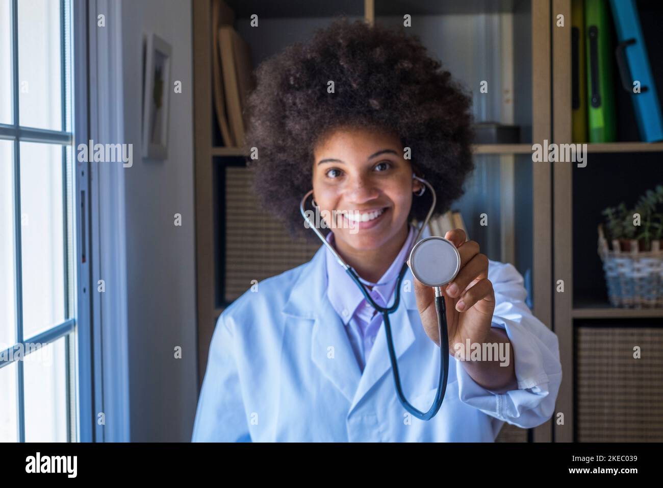 Portrait d'une femme afro-américaine souriante en uniforme montrant un stéthoscope pour vérifier le rythme cardiaque. Un professionnel de la santé montrant l'équipement médical de l'outil d'examen à la caméra Banque D'Images