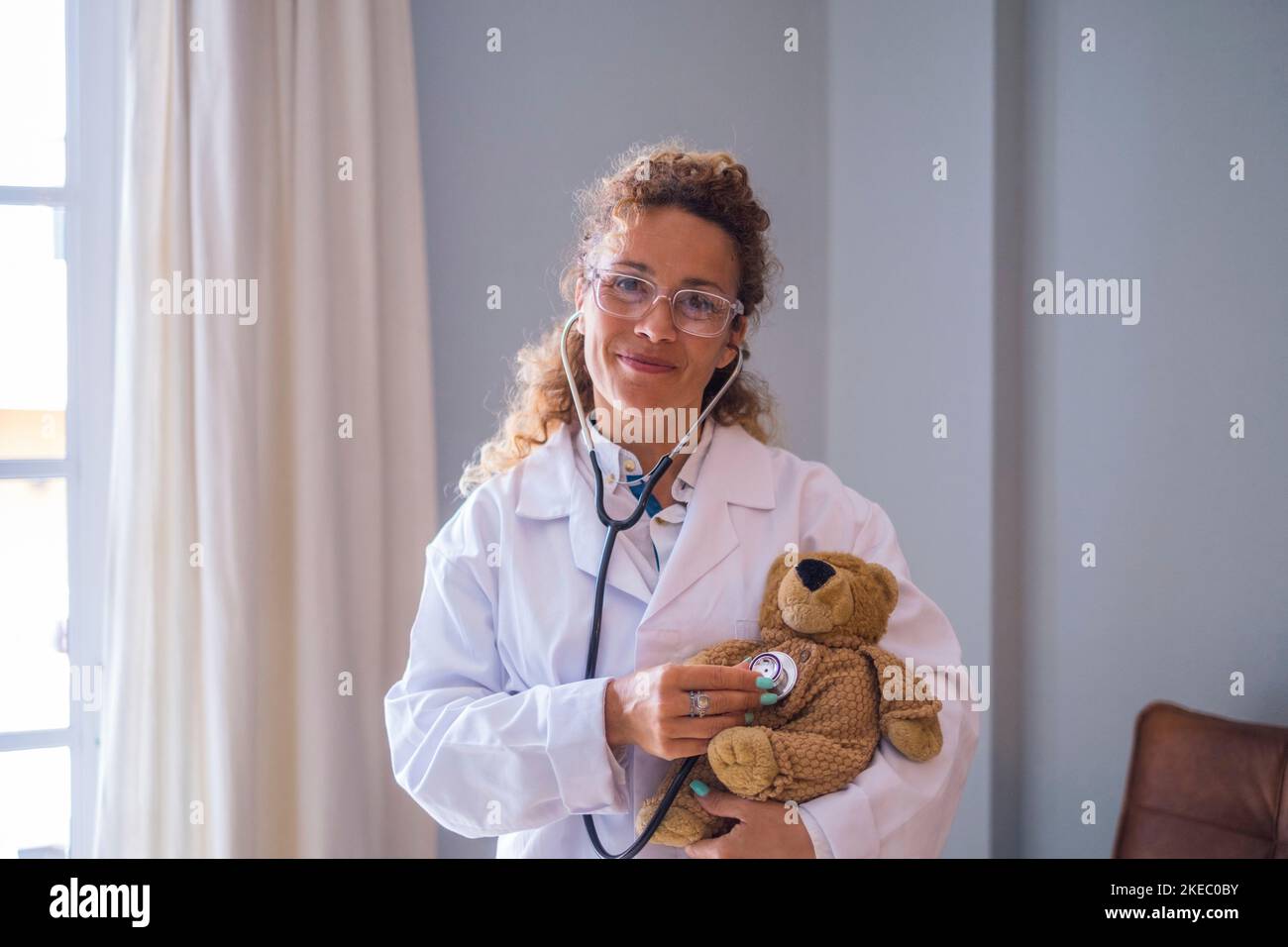 Portriat de jeune femme médecin en uniforme vérifiant l'ours en peluche avec stéthoscope à la clinique. Professionnel de la santé ou professionnel de la santé confiant qui examine l'ours en peluche à l'hôpital Banque D'Images