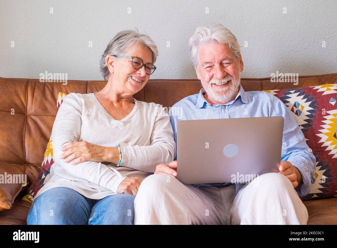 Un couple de personnes âgées gaies utilisant un ordinateur portable tout en étant assis sur un canapé et souriant. Couple de personnes âgées heureux de se détendre en surfant sur un ordinateur portable assis dans le salon. Un vieux couple regarde du contenu multimédia sur un ordinateur portable Banque D'Images