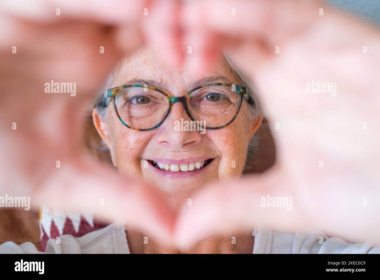 Gros plan d'une femme âgée faisant un geste de forme de coeur avec les mains. Femme âgée heureuse à la retraite qui fait le symbole de la forme du cœur avec ses deux mains et regardant l'appareil photo Banque D'Images