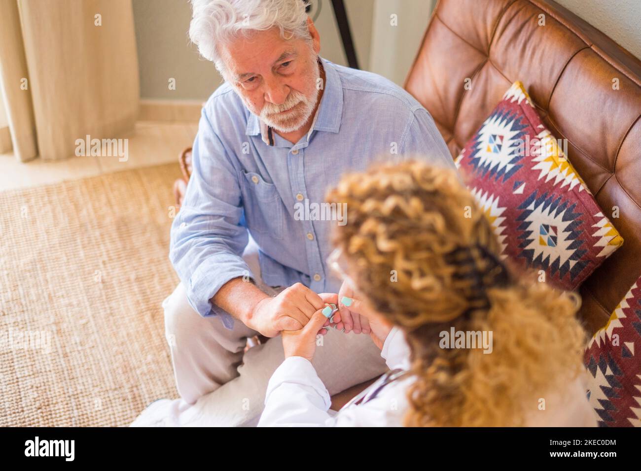 Jeune femme médecin vérifiant et aidant l'homme âgé à sa maison. Médecin aidant le patient âgé et donnant des soins, assis de canapé. Femme aidant à domicile avec un vieil homme à la retraite à la maison Banque D'Images