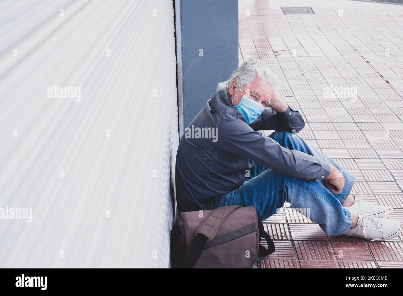 un vieil homme mature assis sur le sol après avoir perdu et fermé son magasin d'activités pour le confinement de quarantaine - retraité senior regardant la caméra portant un masque médical et chirurgical pour prévenir les maladies et covid-19 Banque D'Images