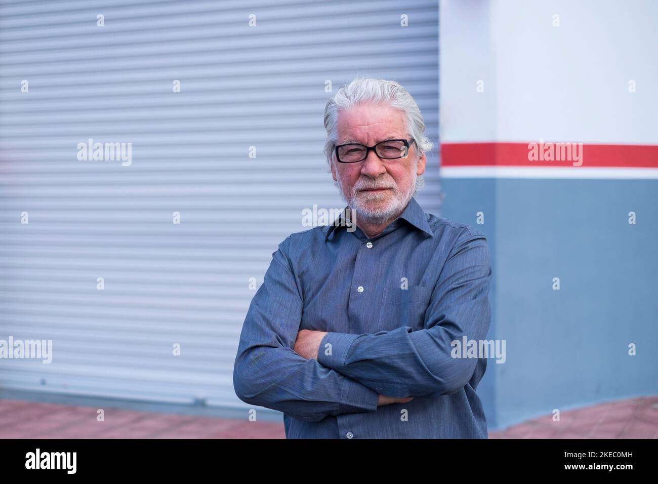 portrait et gros plan d'un vieil homme d'âge mûr regardant l'appareil photo avec à l'arrière son magasin fermé pour le confinement de quarantaine - homme d'affaires professionnel Banque D'Images