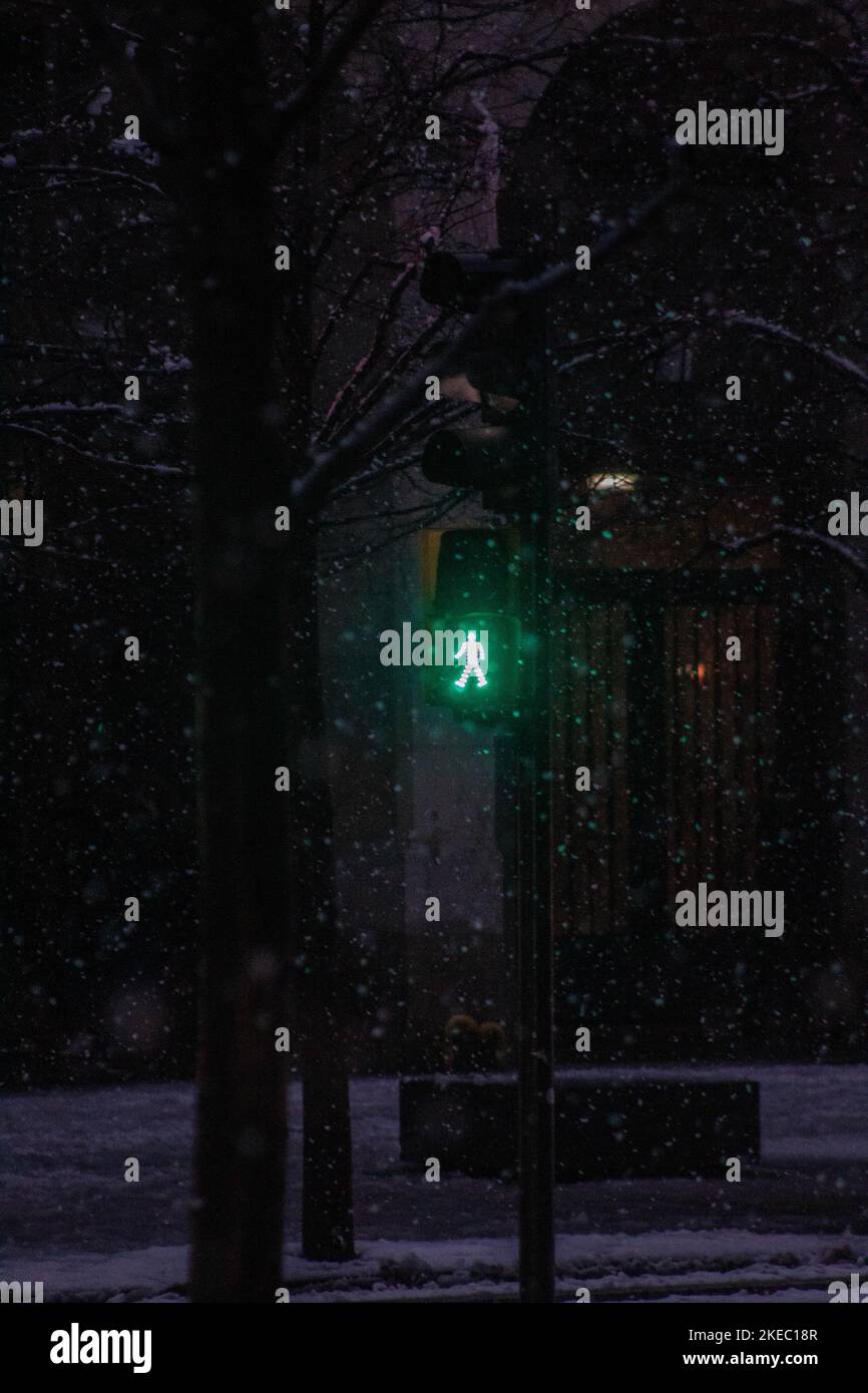 Un panneau vert de marche pour piétons s'allume au crépuscule, visible à travers les flocons de neige Banque D'Images