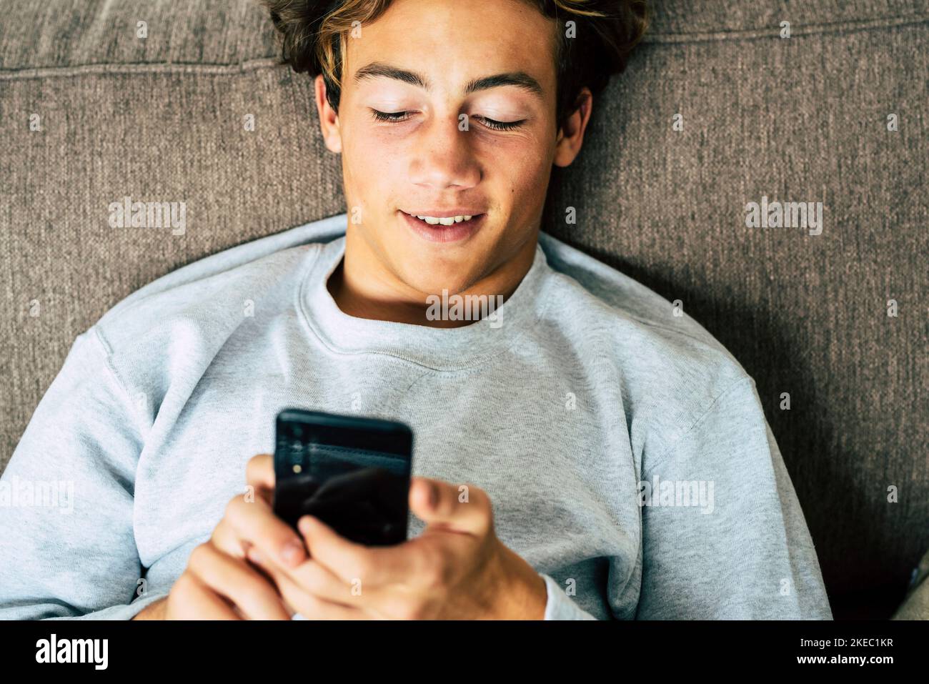 un adolescent à la maison en quarantaine à l'aide de son téléphone et regarder et réviser son réseau social ou ses médias et jouer jeux vidéo sur le canapé - ennuyé homme ou jeune adulte à la maison Banque D'Images