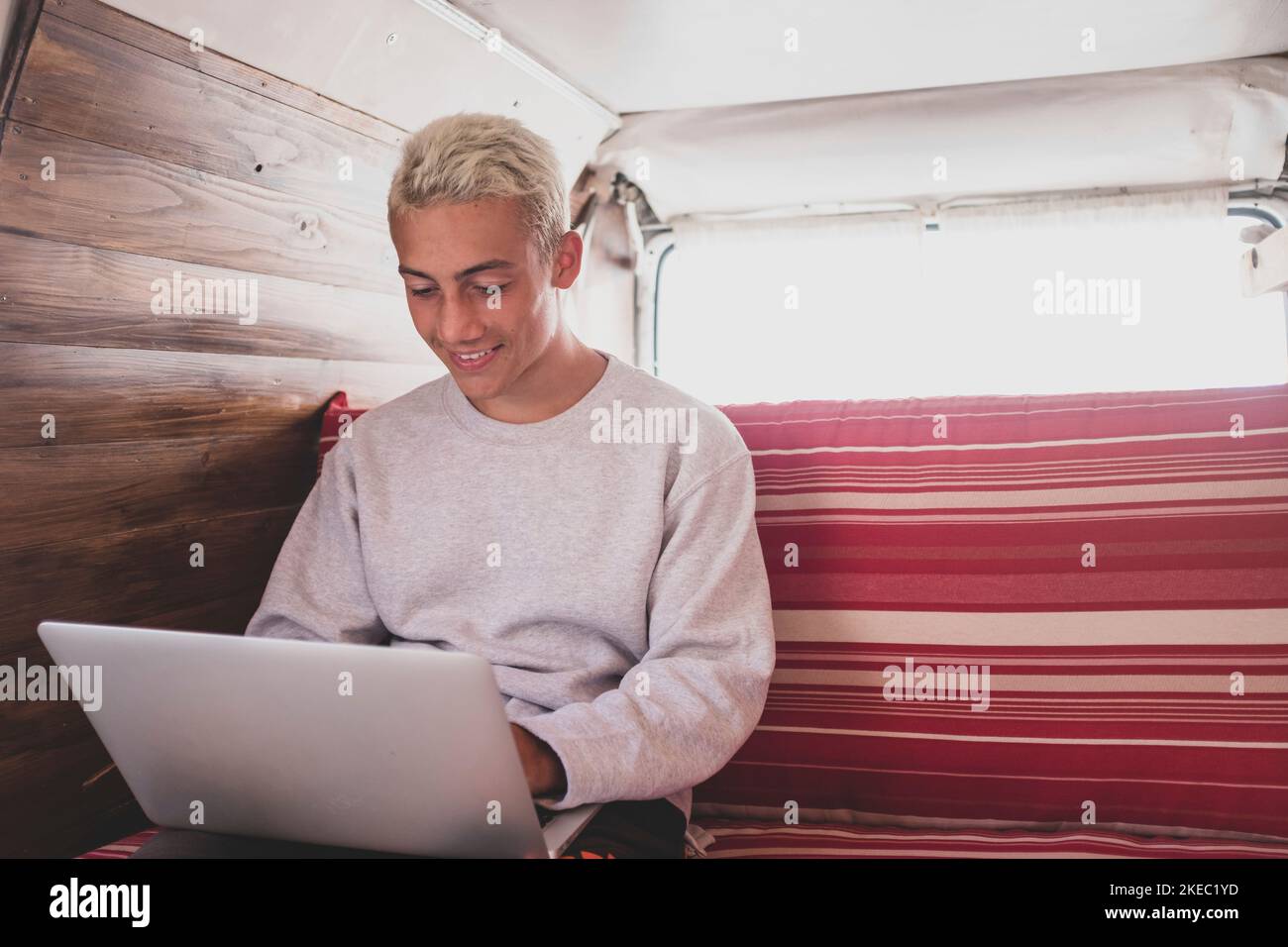 gros plan et portrait d'un jeune homme assis sur le canapé de sa minifourgonnette ou véhicule - à l'aide d'un ordinateur portable et surfer sur le net avec les réseaux sociaux - technologie nomade style de vie Banque D'Images