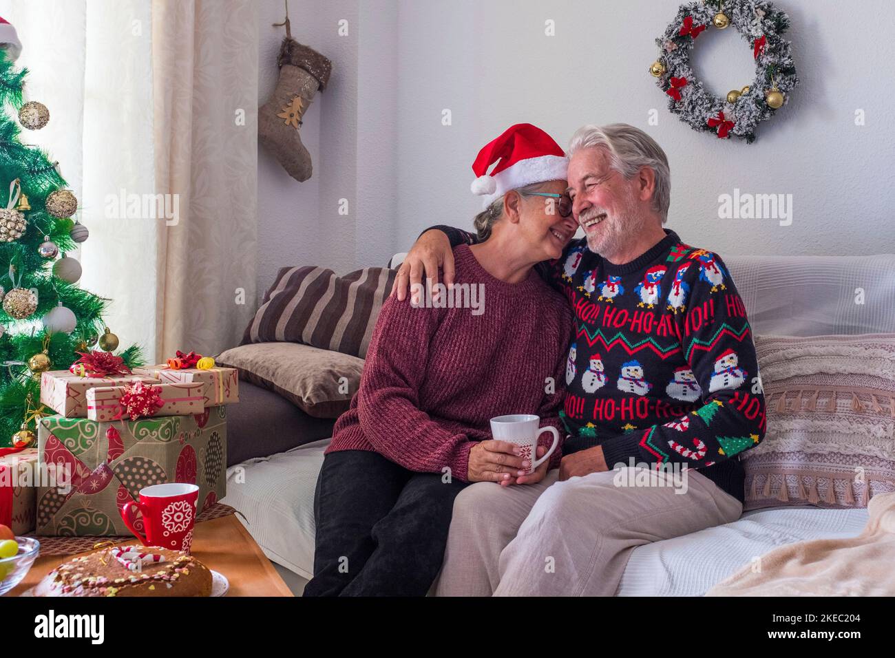 couple de deux aînés heureux et personnes matures assis dans le canapé ayant plaisir ensemble emballer les cadeaux et les cadeaux - pensionnés dans l'amour à la maison Banque D'Images