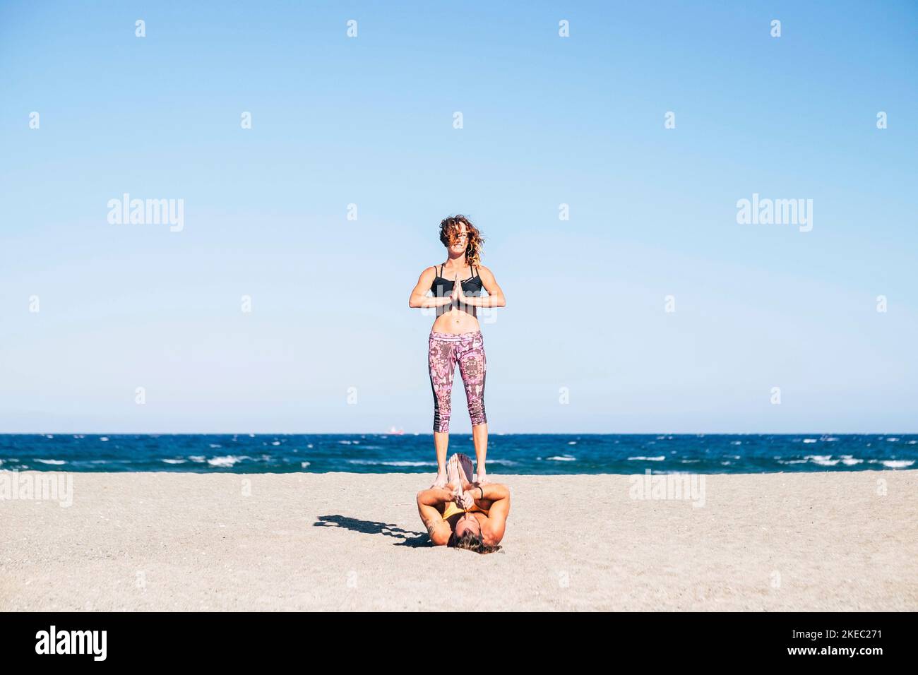 couple de deux adultes faisant acroyoga ensemble à la plage sur le sable - homme tenant son coéquipier avec lui jambes Banque D'Images