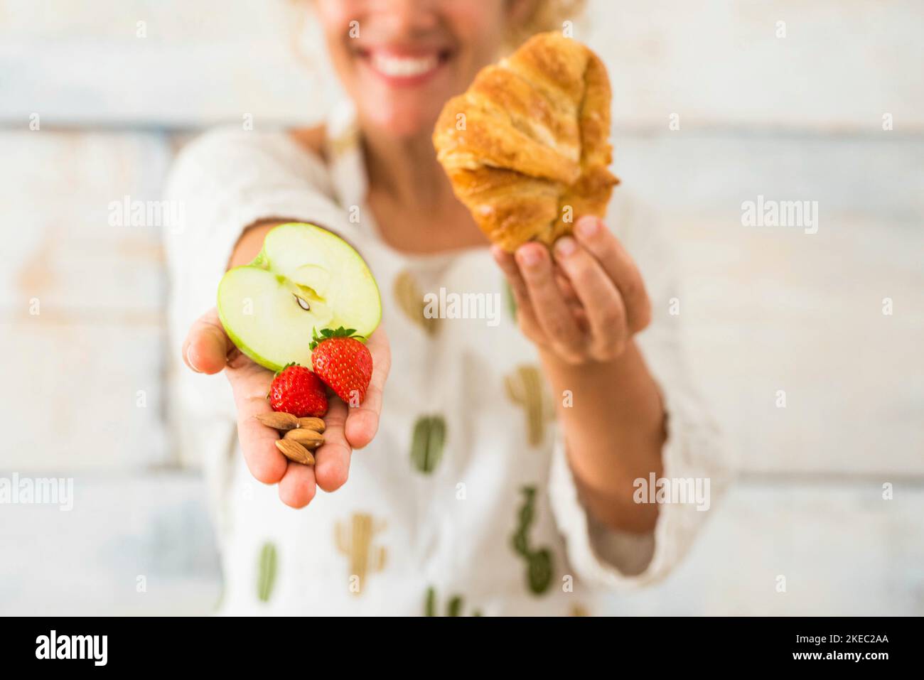 gros plan et portrait de la belle femme montrant à l'appareil photo des aliments sains comme des fruits et dans l'autre main mauvaise alimentation comme croissant Banque D'Images