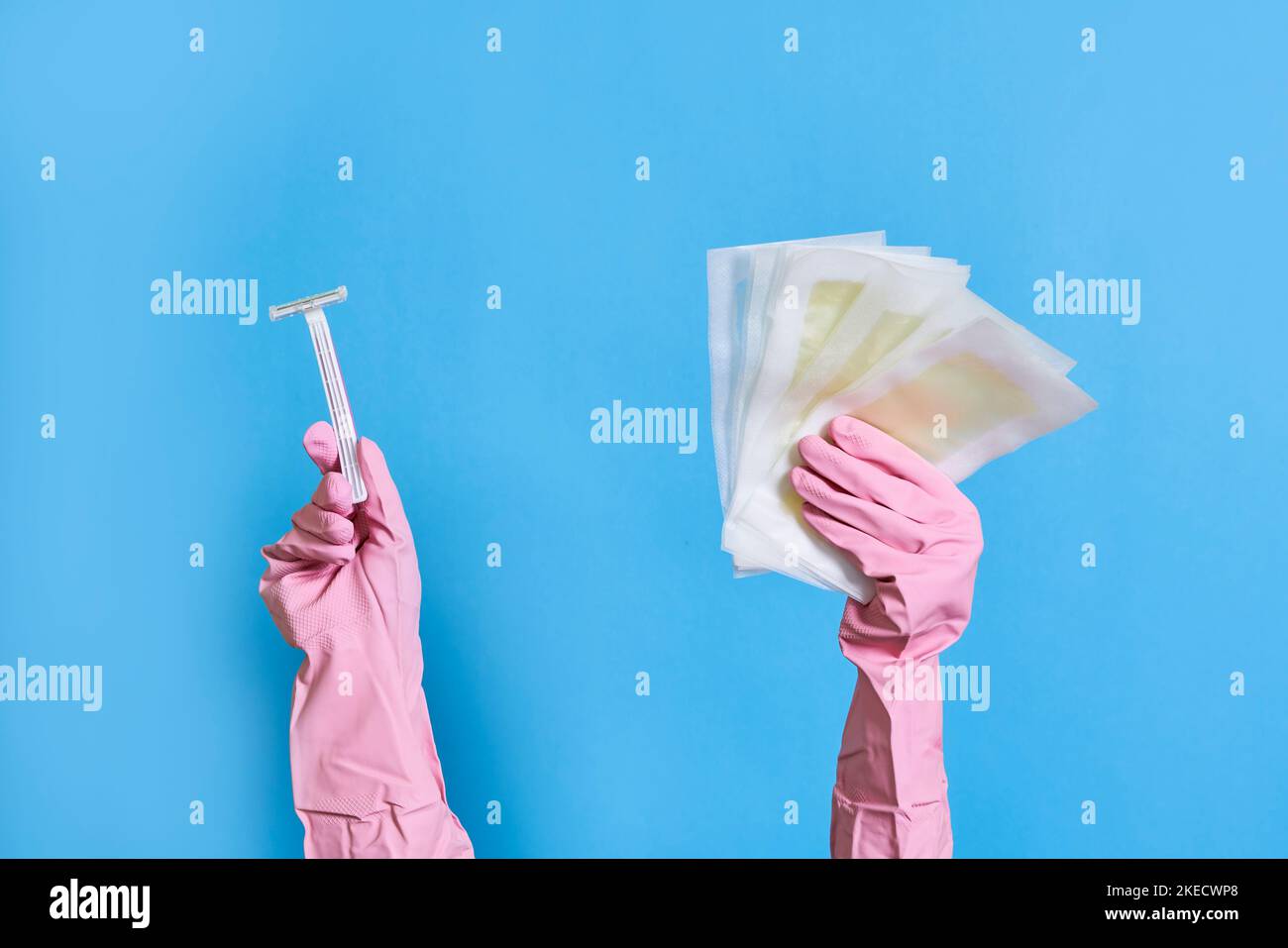 les mains de quelqu'un dans des gants en caoutchouc rose tenant une paire de ciseaux et de chiffons de nettoyage sur un fond bleu Banque D'Images