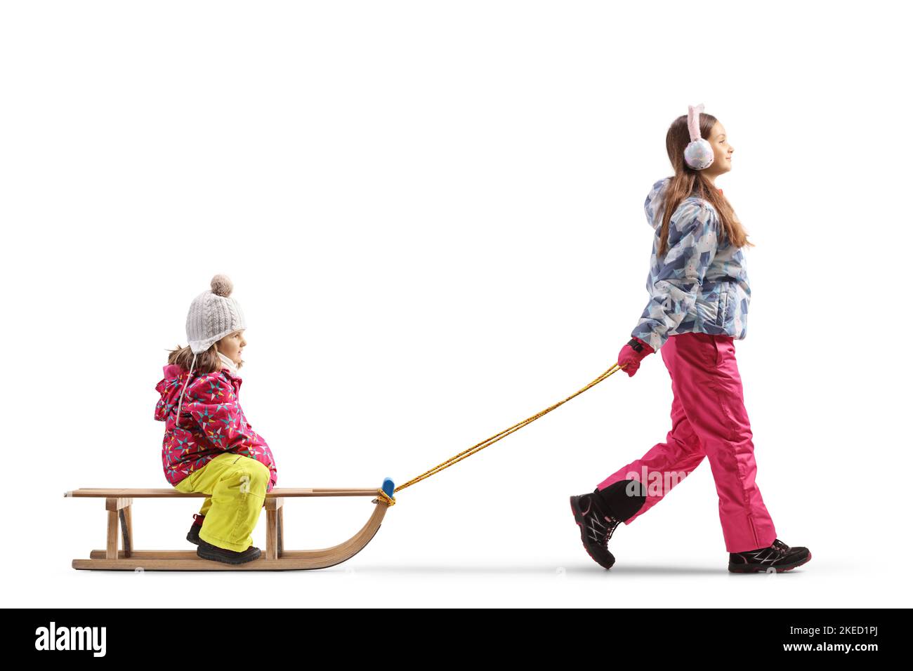 Photo pleine longueur d'une fille tirant un enfant assis sur un traîneau en bois isolé sur fond blanc Banque D'Images