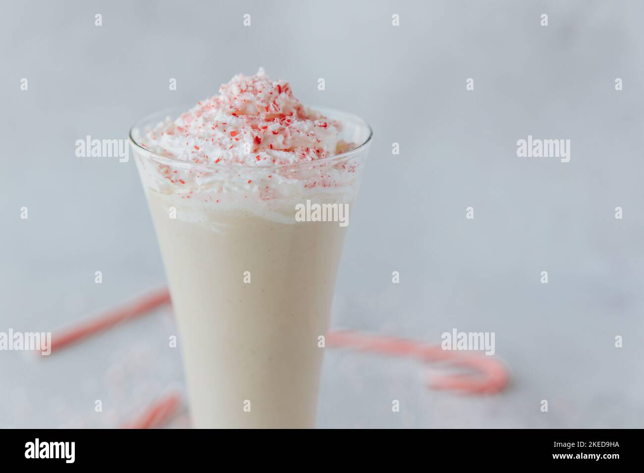 Photo macro d'un verre de bougé de canne à sucre, parsemé de chapelure de canne à sucre, avec des cannes rouges et blanches floues en arrière-plan Banque D'Images