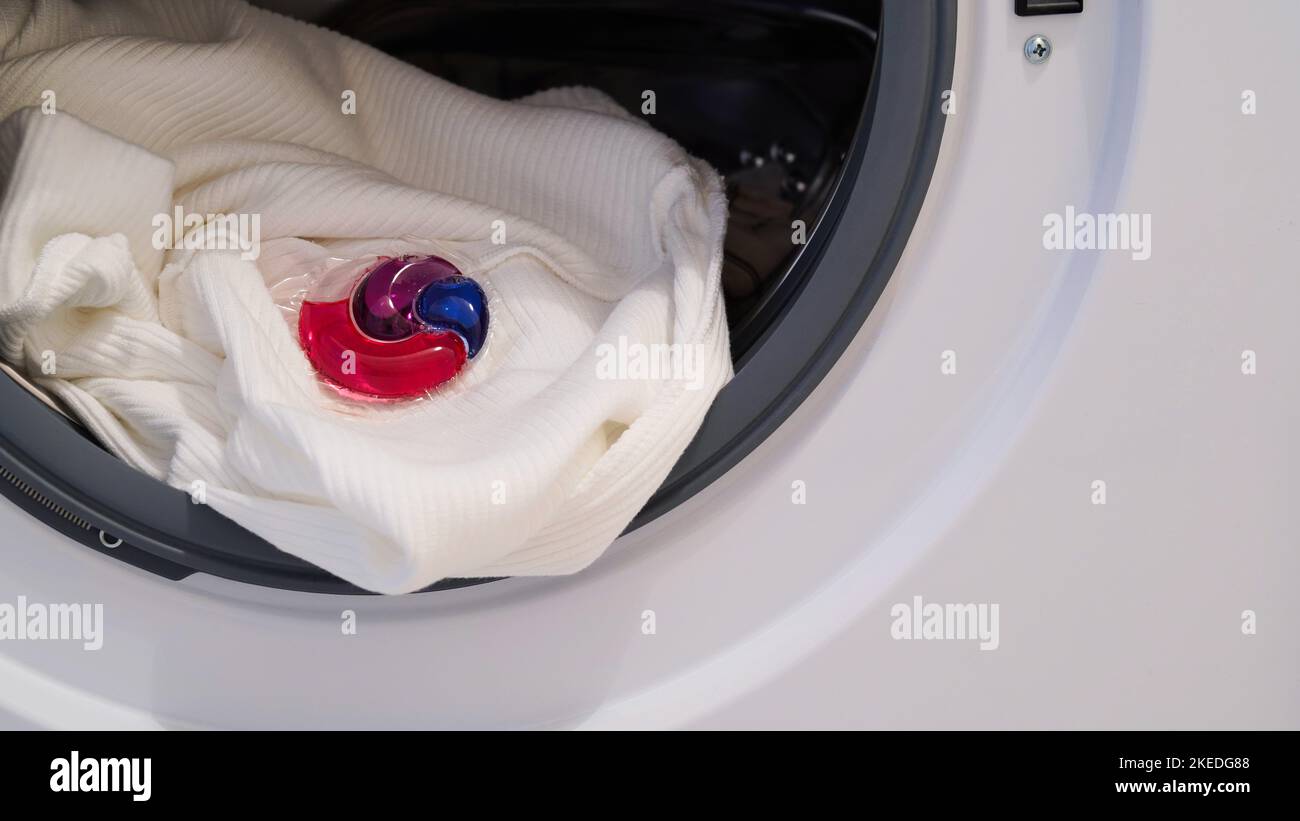 La capsule avec le gel de lavage se trouve dans le tambour de la machine à laver. Gel écologique de blanchisserie coloré en capsule. Clothers de lavage. Banque D'Images