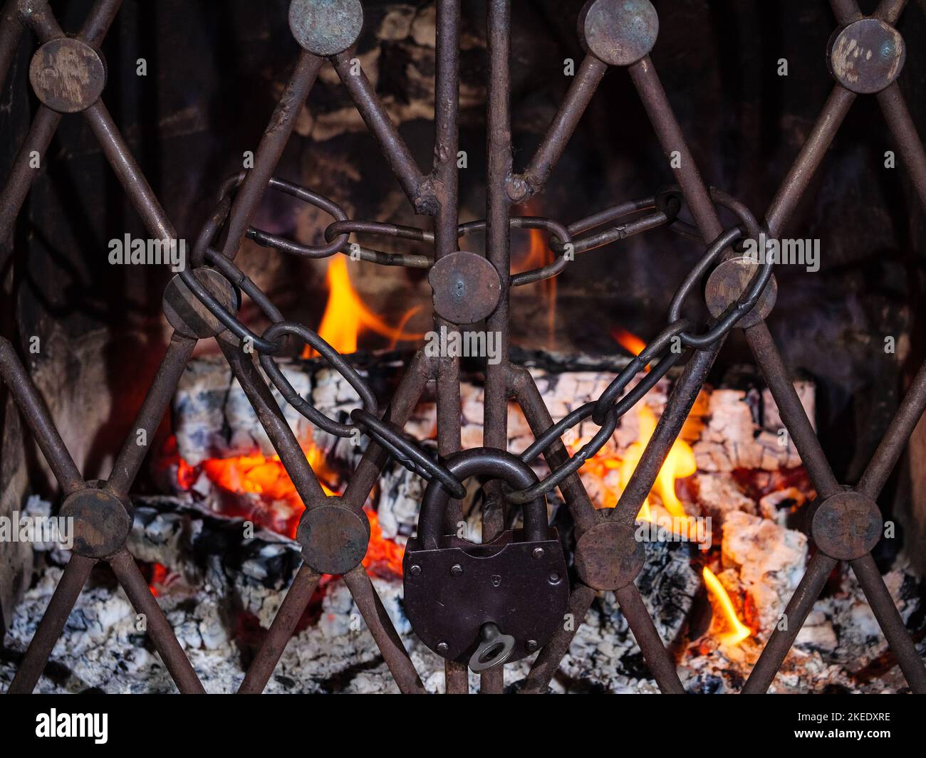 Bois de chauffage brûlé dans une cheminée avec une chaîne et un cadenas derrière une grille verrouillée Banque D'Images