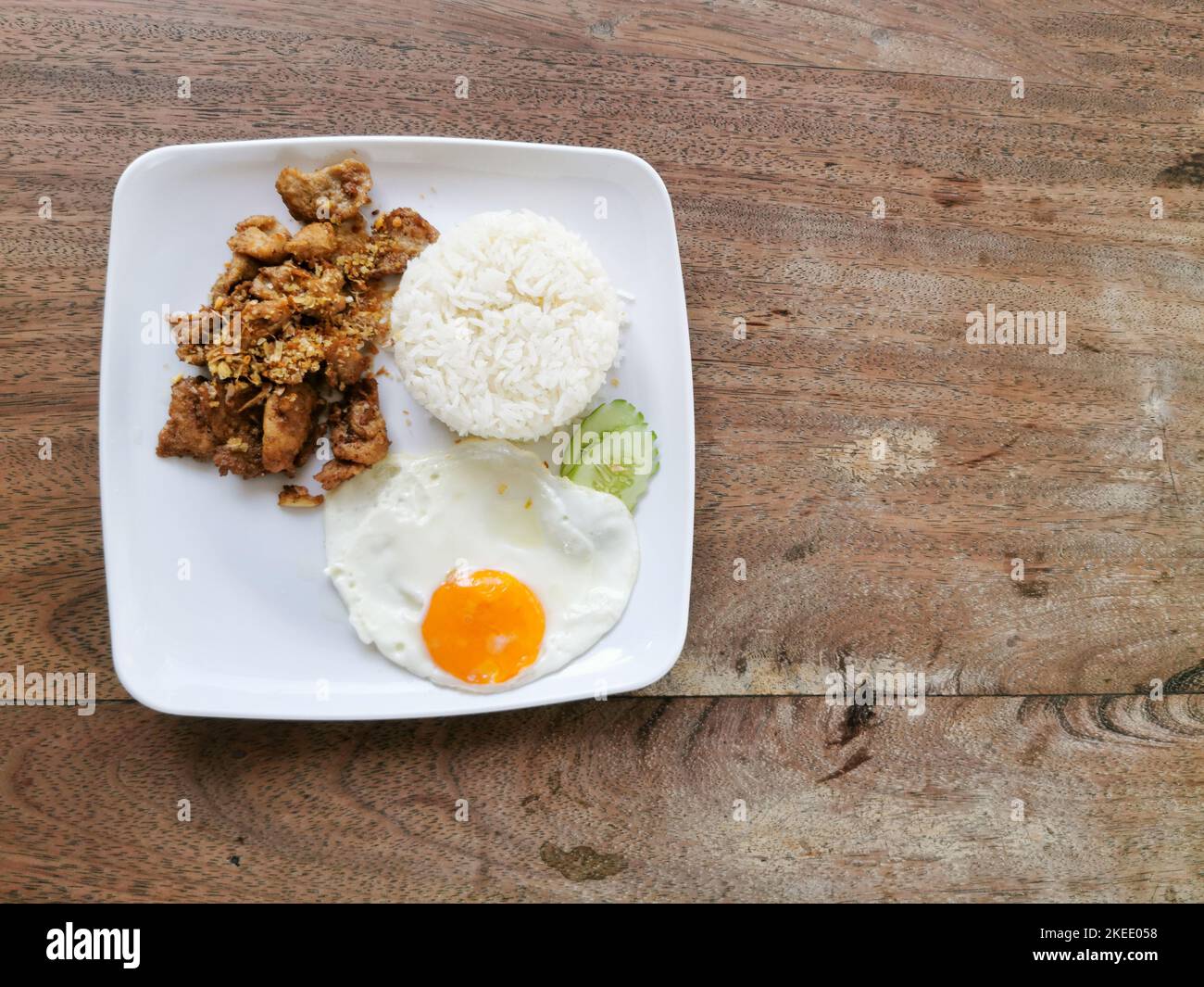 Moo tod kratiem ou gratiem. Porc frite à l'ail et au poivre sur une assiette blanche à fond de bois. Cuisine thaïlandaise de rue en Thaïlande. Banque D'Images