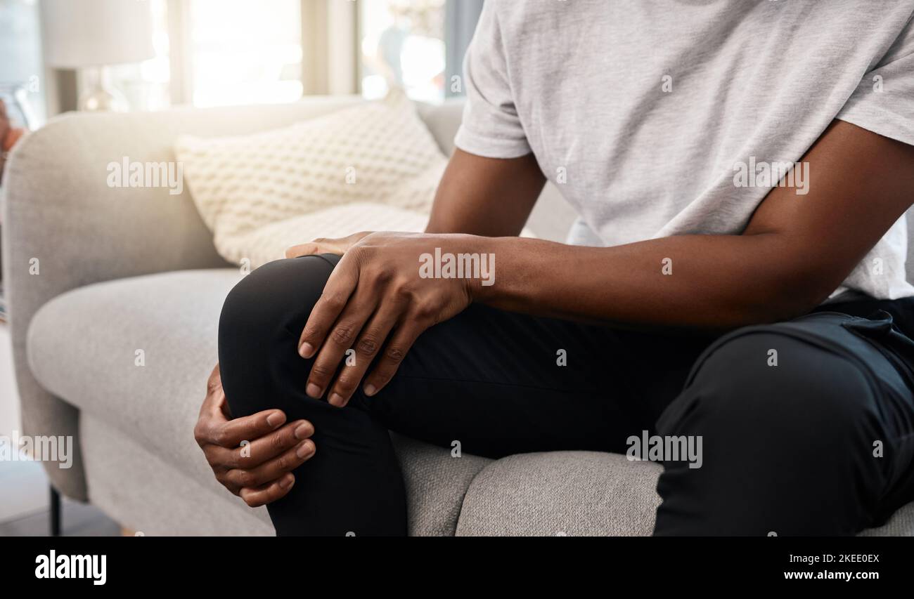 Douleurs au genou, main d'un homme et blessures lorsqu'il est assis sur le canapé de la salle de séjour pour se reposer et se détendre. Douleur, articulation douloureuse de jambe et homme afro-américain Banque D'Images