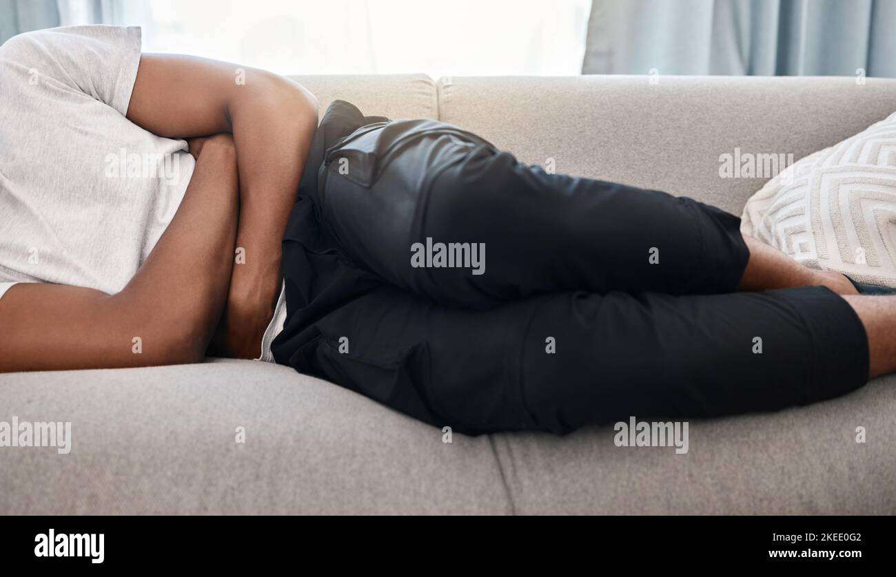 Homme, maux d'estomac et de gros plan allongé sur un canapé dans la salle de séjour à la maison pour le confort, le soulagement ou les soins de santé. Homme noir, repos et détente pour la douleur, constipation ou Banque D'Images