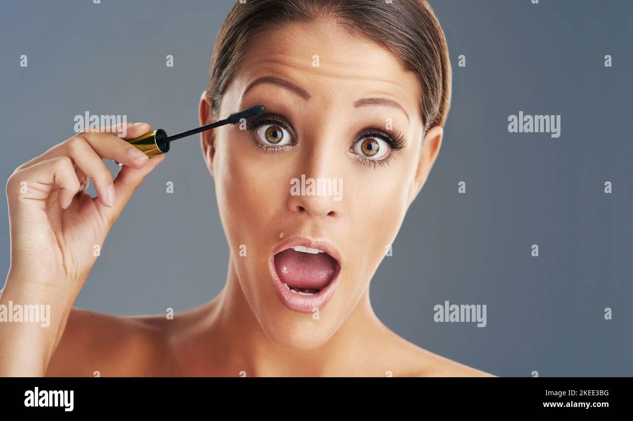 Elle tire ses cils vers le haut. Studio portrait d'une belle jeune femme mettant sur mascara sur un fond gris. Banque D'Images