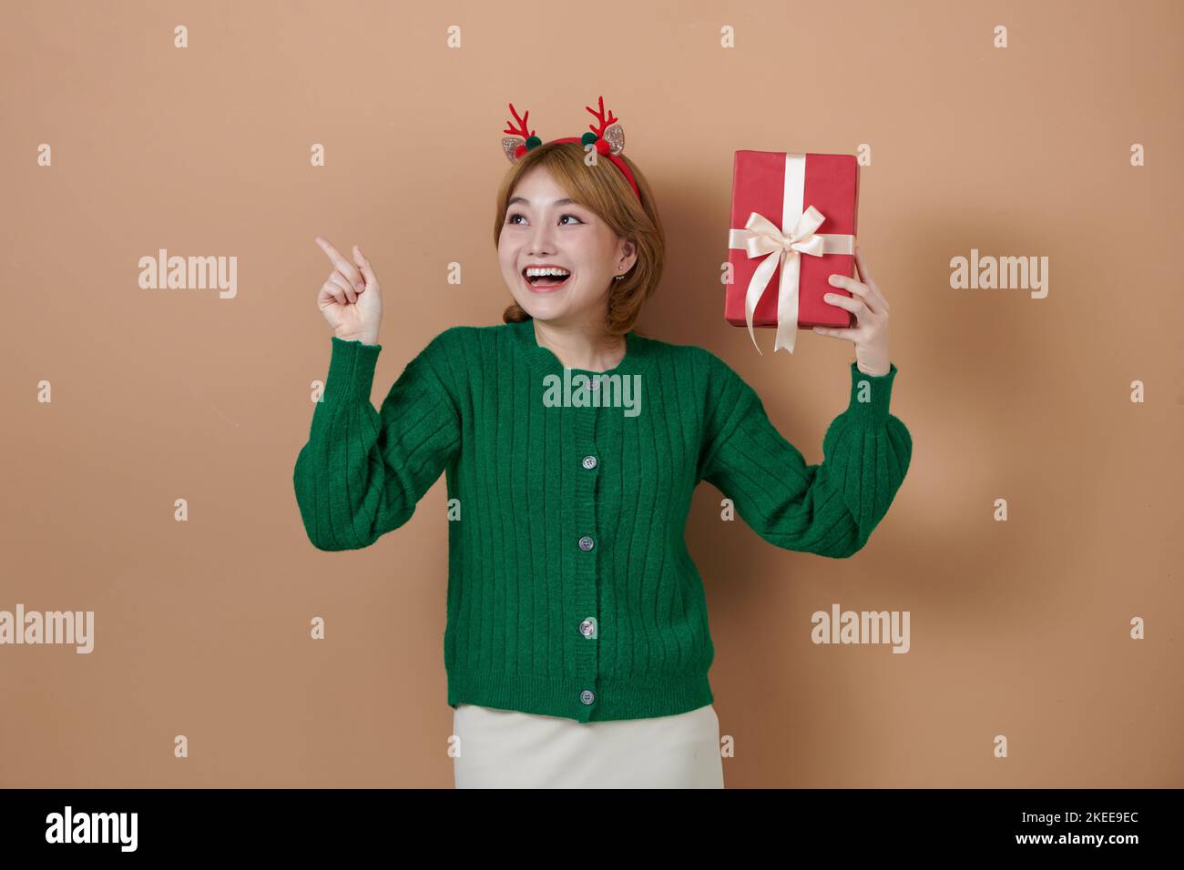 Bonne fille portant des cornes de cerf de Noël tenant une boîte cadeau, pointant sur le côté à l'espace de copie vierge Banque D'Images