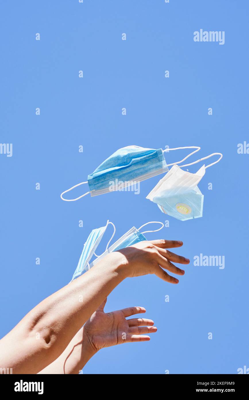 main de quelqu'un tenant une paire de masques chirurgicaux dans l'air contre un ciel bleu sans nuages Banque D'Images